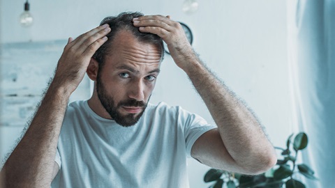 Homem a ver-se ao espelho e a observar a queda de cabelo